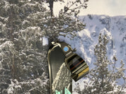 A pair of STAGE Custom Ski goggles hanging from a Nordica Ski. The snow goggles feature the Alaska Avalanche Information Center logo on the strap of the goggle. The model of the goggle is the STAGE Propnetic Magnetic Ski goggle.