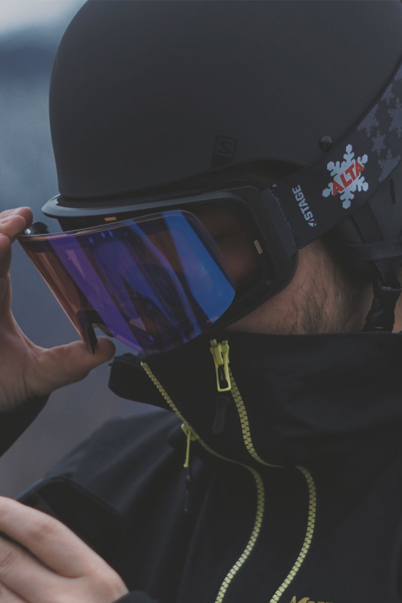 Man changing lenses on his custom STAGE Propnetic magnetic ski goggles featuring an ALTA logo 